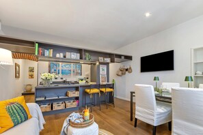 A modern living room with a sofa, a dining table with chairs, a kitchen area with bar stools, and a mounted TV. - Historic Center, 'Piazzetta della Torre' Apartment with Air Conditioning and Wi-Fi (Chiavari)