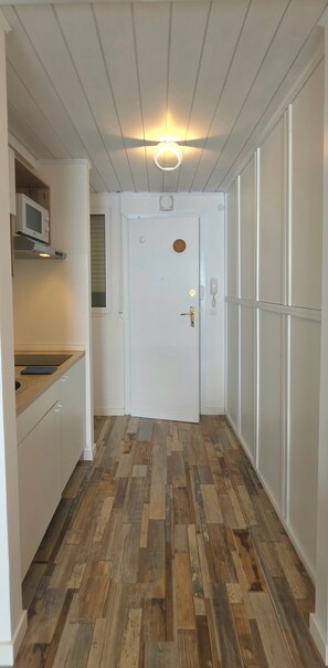 Corredor com porta branca, piso de madeira e micro-ondas sobre bancada.