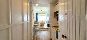 Ein schmaler Flur führt zu einem Essbereich mit Tisch und Stühlen, einer Küche mit Spüle sowie einem Deckenventilator.