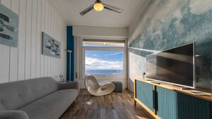 A modern living room with a sofa, a unique chair, a large TV, and a view of the ocean through a window. - "Ocean Blue" – A Gem with Unmatched Sea View, Wi-Fi & Air Conditioning (Sant'Andrea di Rovereto)
