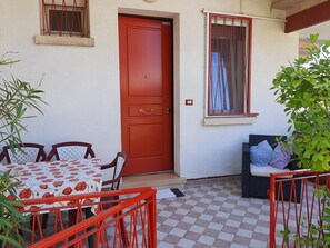 Una puerta roja, un piso a cuadros, una mesa con sillas y una ventana con cortinas.