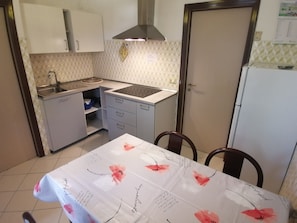 Una cocina compacta con fregadero, estufa y armarios, una mesa de comedor con mantel floral y un refrigerador.