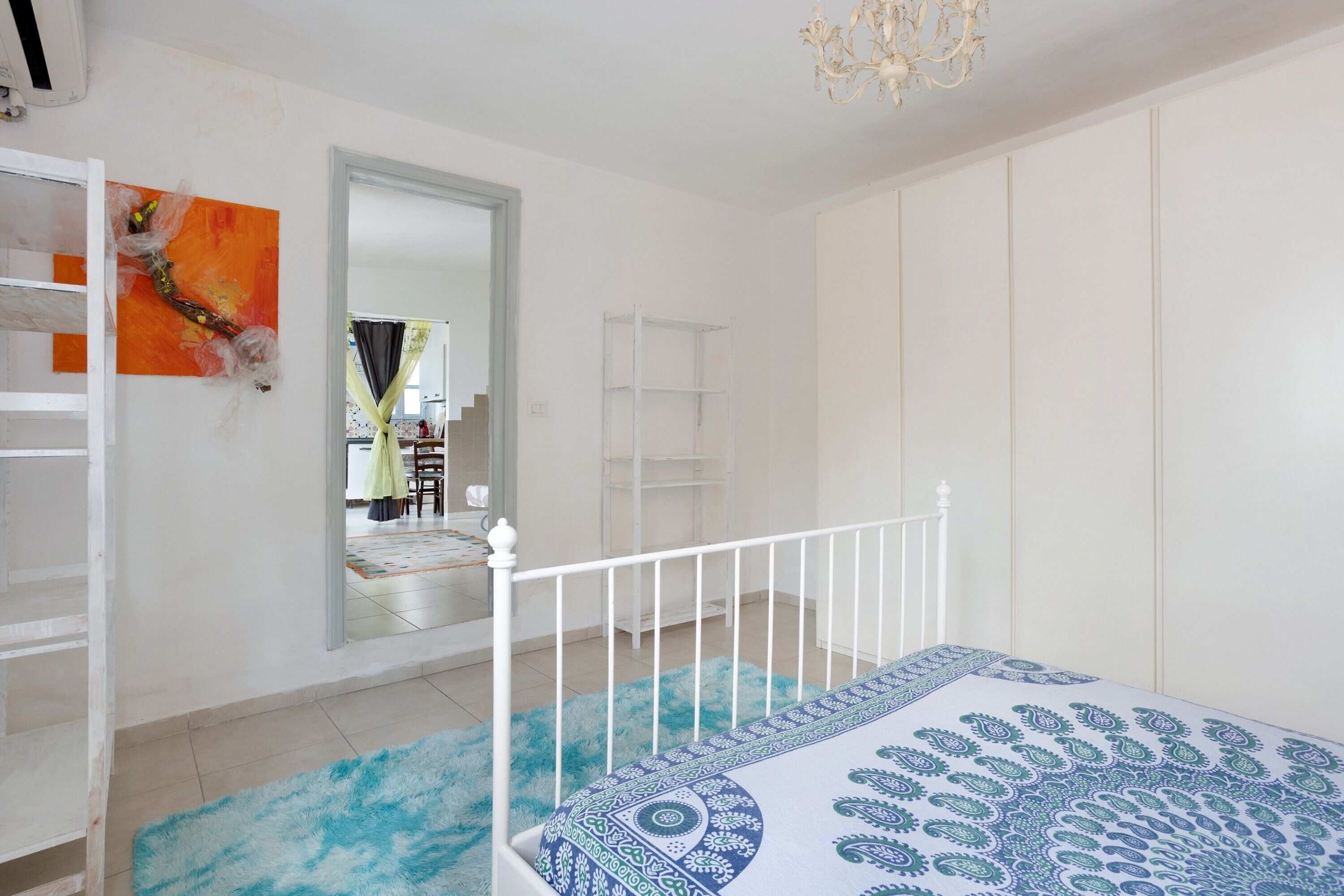 Ein Schlafzimmer mit einem Bett, einem weißen Kleiderschrank, einem Spiegel und einer blauen zudeckenden Bettwäsche.