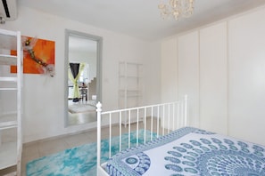 A bedroom with a bed, a white wardrobe, a mirror, and a blue patterned bedspread. - Apartment 'Le Margotte - Rome' with Private Garden, Wi-Fi and Air Conditioning (Stiava)