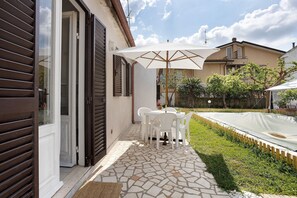 Eine Terrasse mit Tisch und Stühlen, einem weißen Sonnenschirm und einem Boden aus Steinplatten.