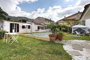 Ein Wohnhausgarten mit kleinem Pool, einem weißen Tisch, Topfpflanzen und einem weißen Zelt.