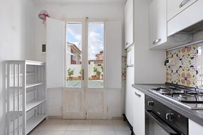 A kitchen with a gas stove, white cabinets, a tiled backsplash, and a door leading to a balcony. - Apartment 'Le Margotte - Rome' with Private Garden, Wi-Fi and Air Conditioning (Stiava)