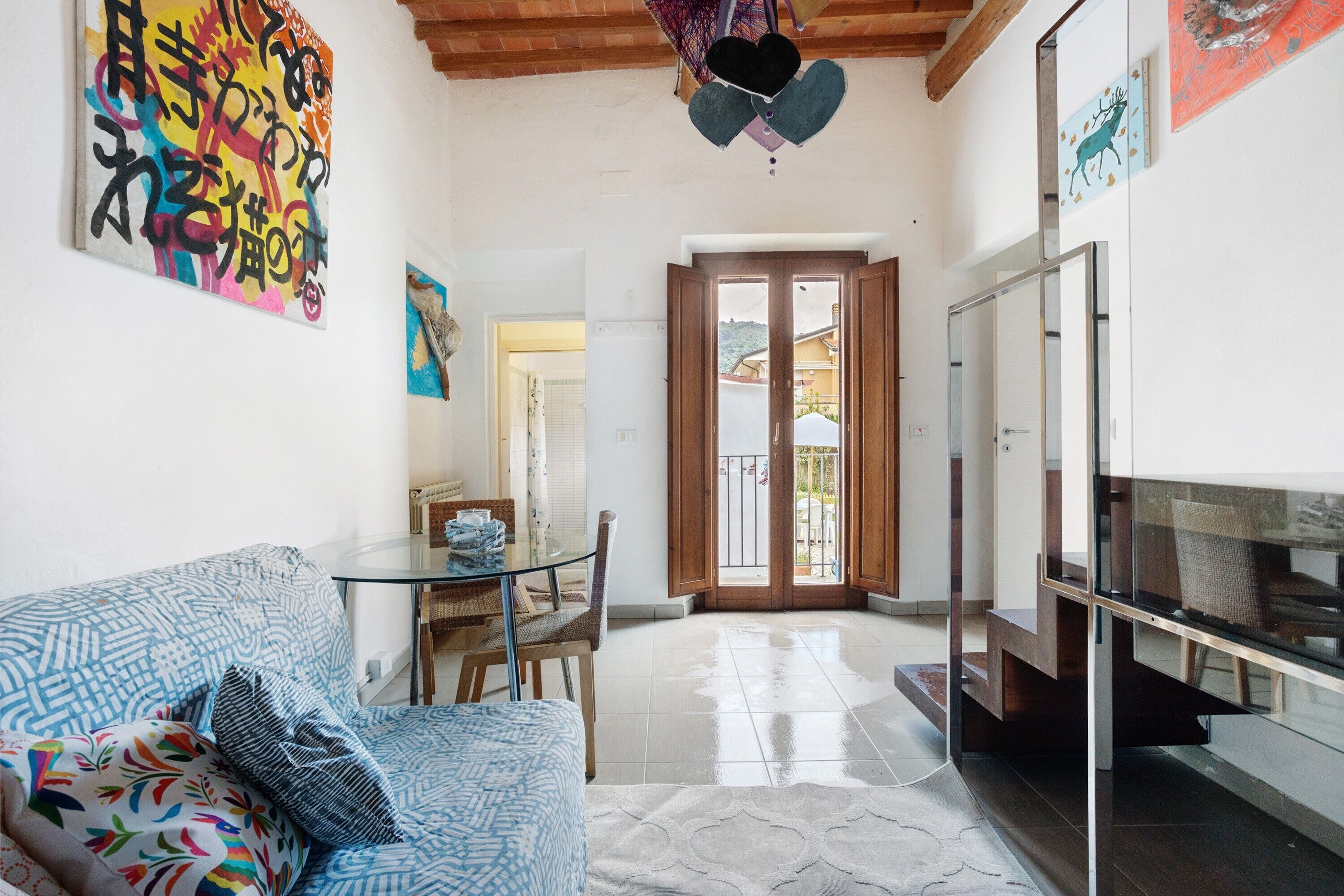 A living room with a sofa, a glass table, and a TV. There is a door leading to an outdoor area.