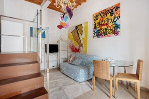 A living room with a sofa, two wicker chairs, a glass table, a TV, and a staircase. - Holiday Home 'Le Margotte - Apartment Lola' with Garden, Wi-Fi and Air Conditioning (Stiava)