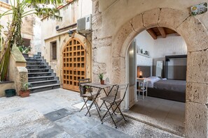 Une terrasse extérieure avec une table et des chaises, une porte en bois et un escalier menant à une pièce comprenant un lit et une table de chevet.