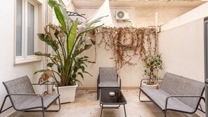 En terrasse med to grå stole, et lille bord og krukker med planter.