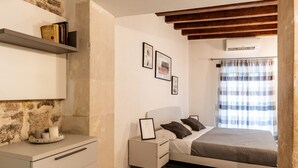 A bedroom with a bed, bedside table, wall-mounted shelf, and a crib. - La Naca by Wonderful Italy (Syracuse)
