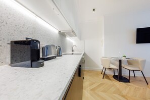 Eine moderne Küche mit Marmorarbeitsplatte, einer Kaffeemaschine, einem Toaster und einem Wasserkocher. Es gibt einen Essbereich mit Tisch und Stühlen.