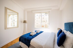 A hotel room with a bed, a large mirror, a floor lamp, and a window with a view of buildings. - Premium 1-Bedroom - Trocadéro - Eiffel Tower - Paris 16 (Paris)