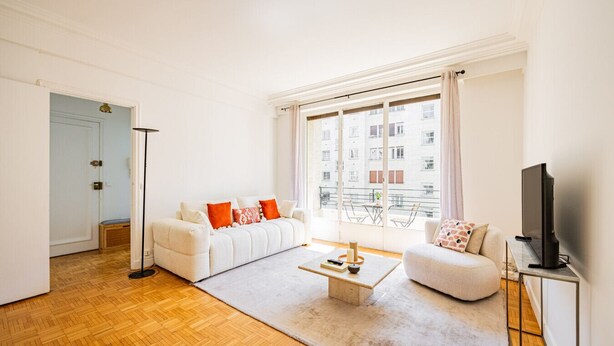 Ein Wohnzimmer mit einer Couch, einem Couchtisch, einem Fernseher und einem großen Fenster mit Blick auf Gebäude.