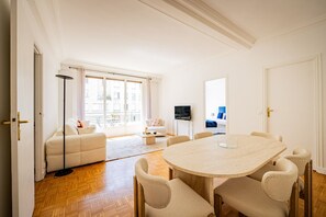 A spacious living area with a round table, sofa, and a television. - Premium 1-Bedroom - Trocadéro - Eiffel Tower - Paris 16 (Paris)