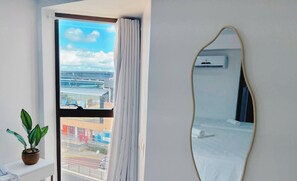 Ein Hotelzimmer mit großem Fenster, einem Blumentopf, einem Spiegel und einer Klimaanlage.