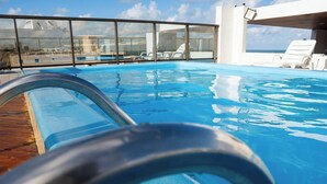 Una piscina con barriera in vetro, lettini e vista sull'oceano.