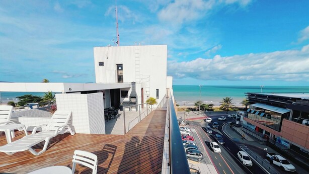 Un edificio moderno con una terrazza sul tetto, vista sull'oceano e una strada trafficata qui sotto.