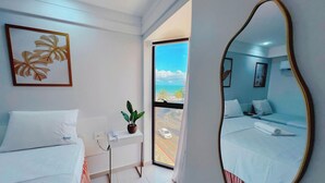 Una camera d'albergo con un letto, un comodino con una pianta, uno specchio e una finestra vista mare.