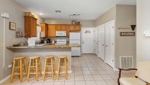 A kitchen with wooden cabinets, a microwave, a refrigerator, and a bar area with stools.