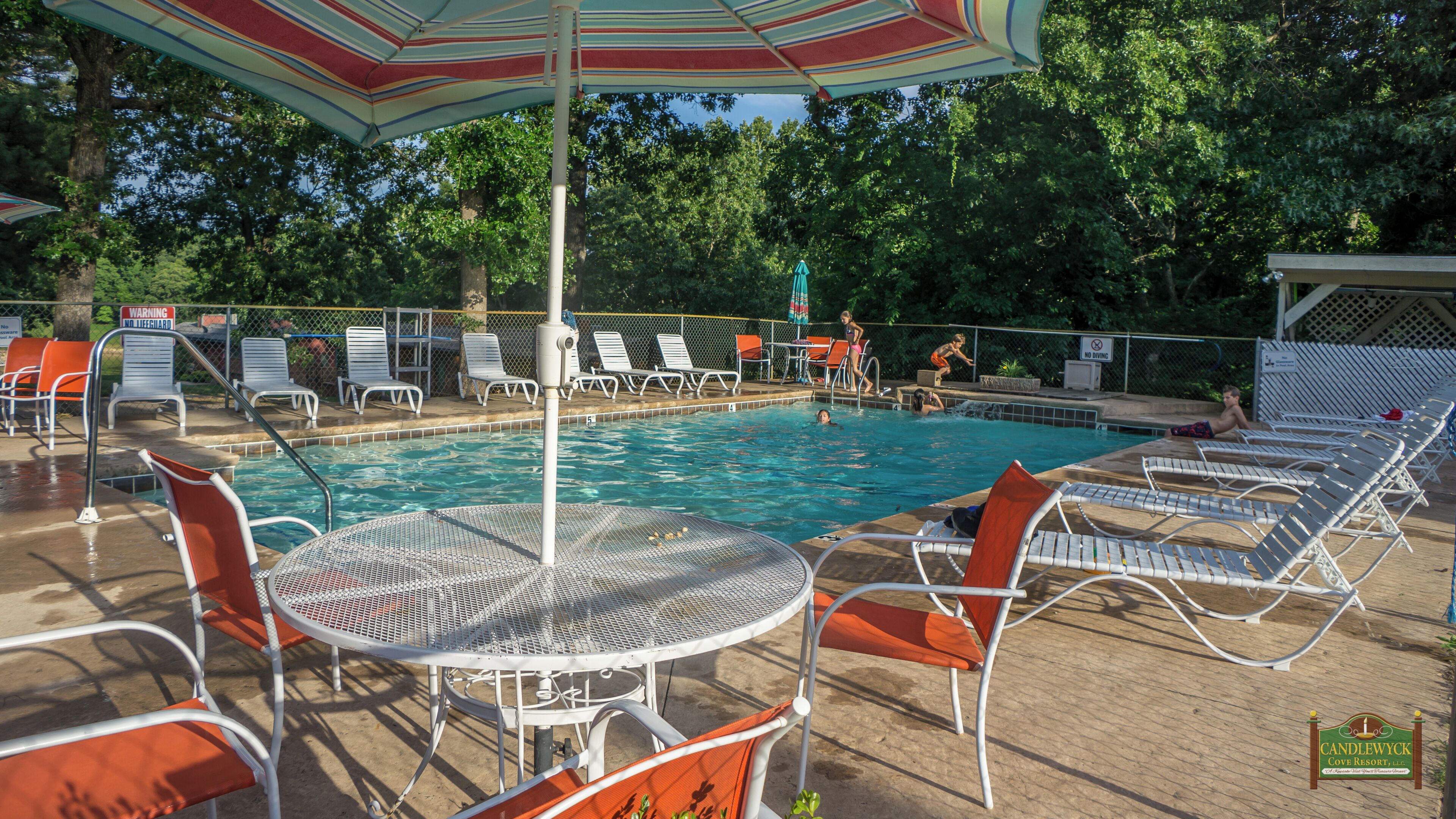A pool area with lounge chairs, a table, and umbrellas.