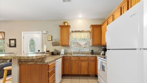 A kitchen with wooden cabinets, a white refrigerator, a granite countertop, and a window with a curtain.
