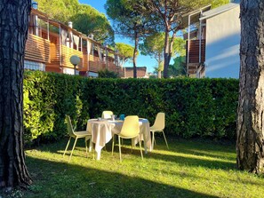 A patio with a table and chairs, surrounded by a hedge and trees. - Enchanting Villa for six Guests (Lignano Sabbiadoro)