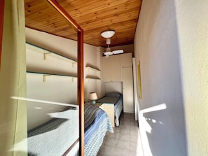 A narrow corridor with wooden ceiling and walls, leading to a room with a bed, a lamp, and a refrigerator. - Enchanting Villa for six Guests (Lignano Sabbiadoro)