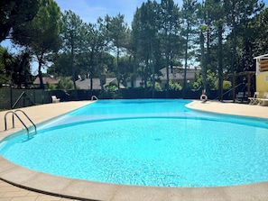Une piscine aux eaux cristallines, dotée d’un escalier en métal, entourée d’une terrasse dallée et d’arbres.