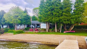Une jetée en bois s’étendant sur une étendue d’eau, avec une maison et des arbres en arrière-plan.