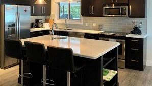Une cuisine moderne avec des meubles de couleur sombre, des appareils en acier inoxydable et un îlot central doté de tabourets de bar.