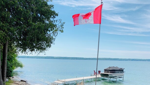 Une terrasse au bord du lac, avec des fauteuils Adirondack rouges, un foyer et un drapeau canadien.