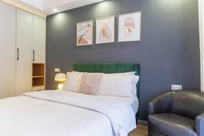 A bedroom with a bed, a green headboard, a bedside table with a lamp, and a chair. There are three framed pictures on the wall. - Atelier Luxe Home, Charming Modern Styled 1bedroom in Kileleshwa (Nairobi)