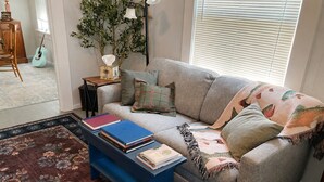 A living room with a sofa, a blue coffee table with books, a lamp, and a guitar. - Mt. Shasta Basecamp. Walkable downtown. Near Waterfalls, Castle Crags & Fishing. (Dunsmuir)