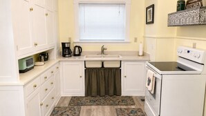 A compact kitchen with white cabinets, a sink, a stove, and a window with blinds. - Mt. Shasta Basecamp. Walkable downtown. Near Waterfalls, Castle Crags & Fishing. (Dunsmuir)