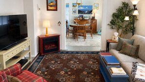 A living room with a television, fireplace, sofa, and a dining area with chairs and a table. - Mt. Shasta Basecamp. Walkable downtown. Near Waterfalls, Castle Crags & Fishing. (Dunsmuir)