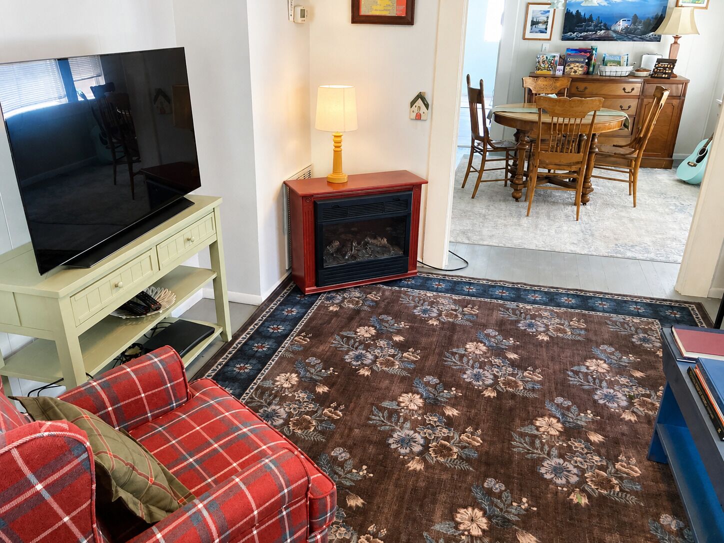 Ein Wohnzimmer mit Fernseher, Kamin, Essbereich und einem gemusterten Teppich.
