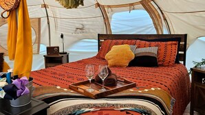 A tent with a bed, pillows, a tray with glasses, and a radio. - Cuddly cow yurt with fluffy cows, llamas, and sheep (Thomson)