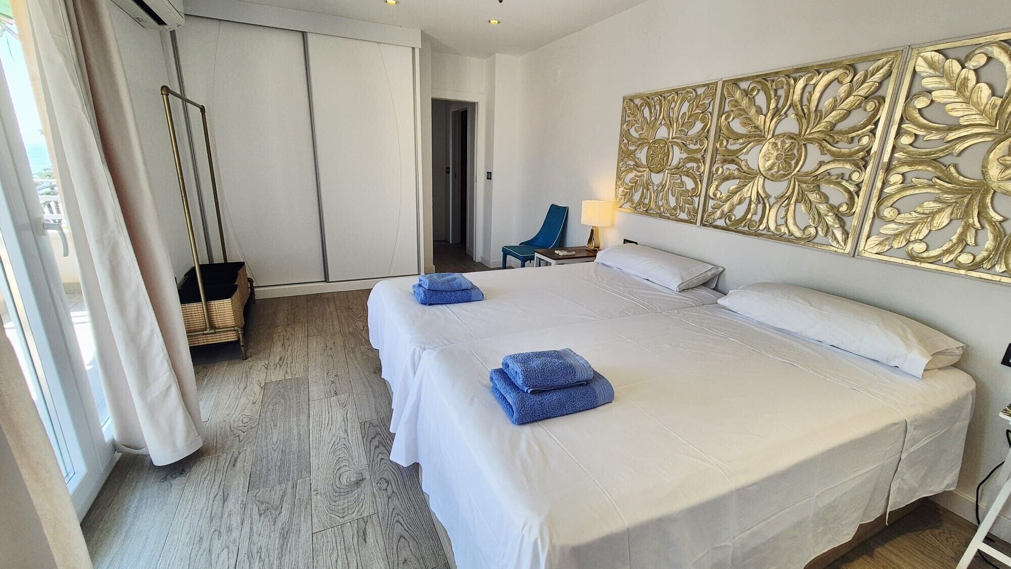 A hotel room with a large bed, a wardrobe, a chair, and a decorative wall panel.