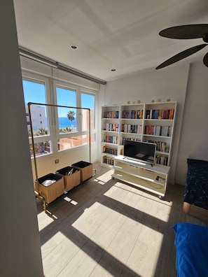 Une pièce dotée d’une grande fenêtre, d’une bibliothèque, d’un téléviseur et d’un ventilateur de plafond.
