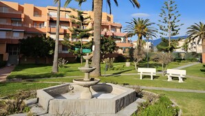 A courtyard with a central fountain, palm trees, and a building with balconies in the background. - Apartment 'Duplex Jardines Del Mar' with Sea View, Wi-Fi and Air Conditioning (Salobreña)