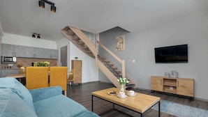 Ein modernes Wohnzimmer mit einem blauen Sofa, einem Holztisch und einer Treppe, die in einen Küchenbereich führt.
