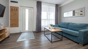 Ein modernes Wohnzimmer mit einer Couch, einem Couchtisch, einem Holzkabinett, einem Fernseher und einem großen Fenster mit Vorhängen.