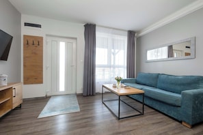 Ein modernes Wohnzimmer mit einer Couch, einem Couchtisch, einem Holzkabinett, einem Fernseher und einem großen Fenster mit Vorhängen.
