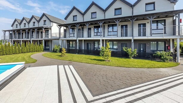 Ein modernes Hotel mit mehreren Balkonen, einem Schwimmbad und einem gepflegten Rasen.