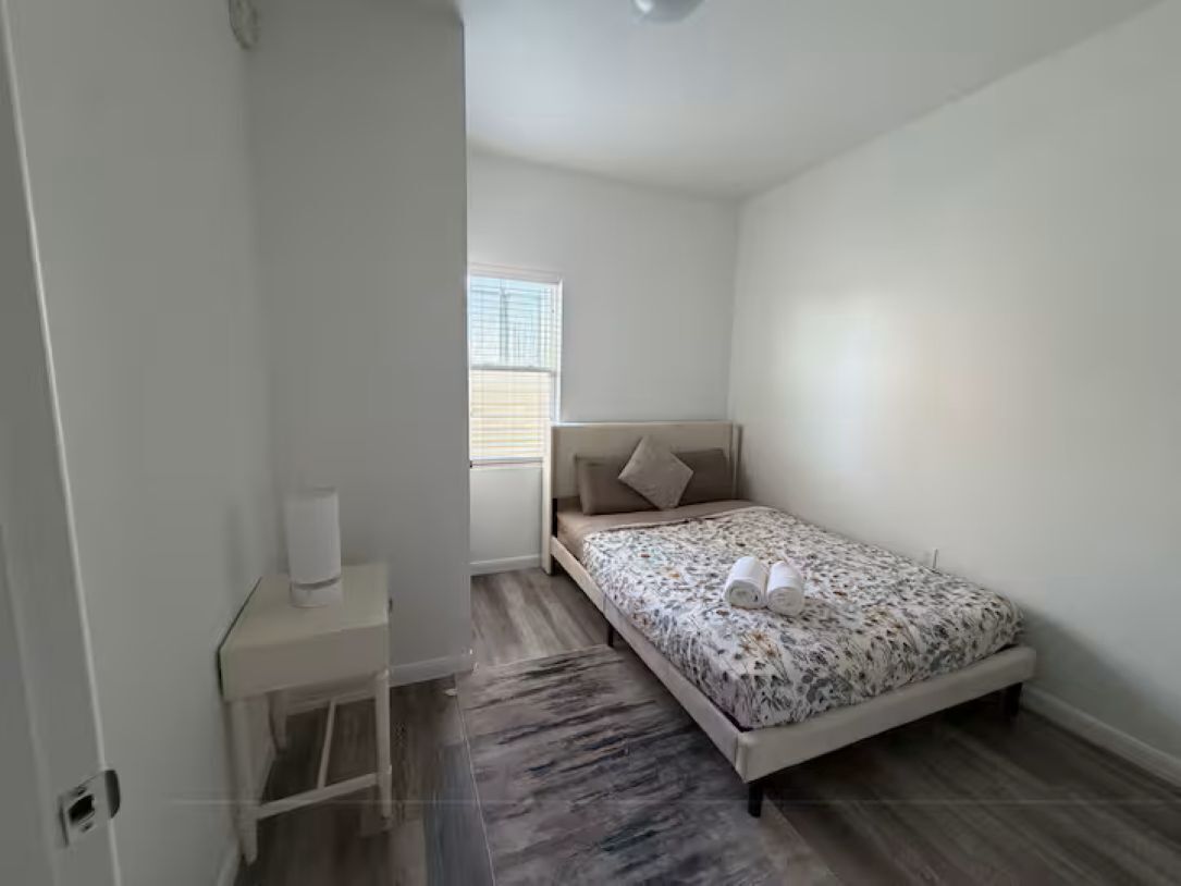 A bedroom with a bed, a bedside table, a window, and a door.