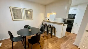 Cocina compacta con comedor, piso de madera y una pequeña isla con taburetes.