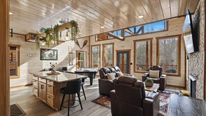 Ein geräumiges Blockhütten-Interieur mit Holzausstattung, einem Billardtisch, Ledersitzmöbeln und großen Fenstern.