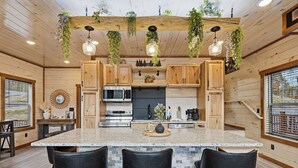 Eine Küche mit Holzausstattung, einer Granit-Arbeitsplatte, hängenden Pflanzen und einer zentralen Kochinsel mit Barhocker.